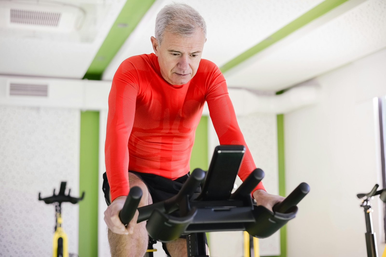 Senior man in red activewear exercising on stationary bike indoors, promoting healthy lifestyle.